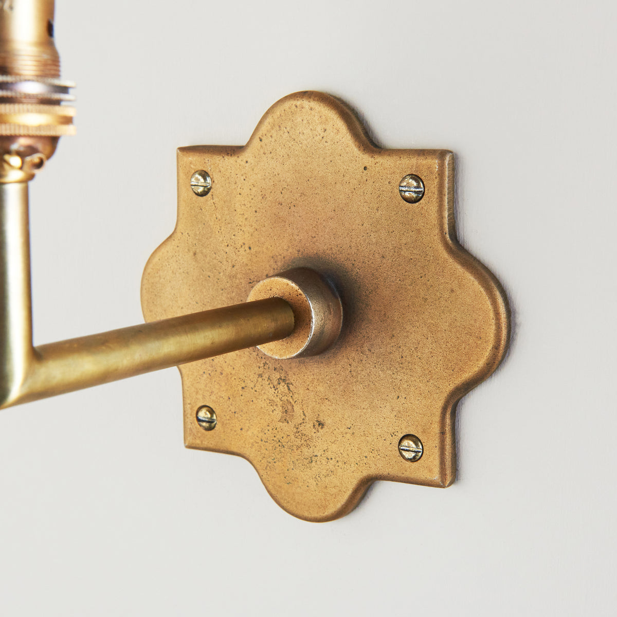 Detail of the Anvil Angle wall light's scalloped antique brass backplate and slim straight arm