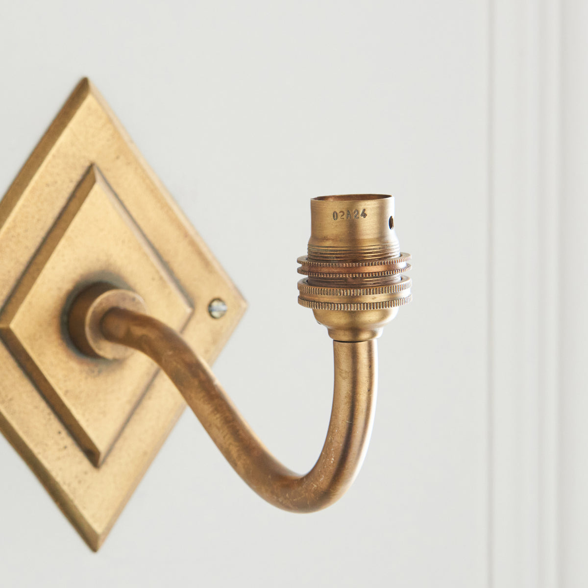 Close-up of the brass bulb holder at the end of the Diamond Curve wall light's swan-neck arm