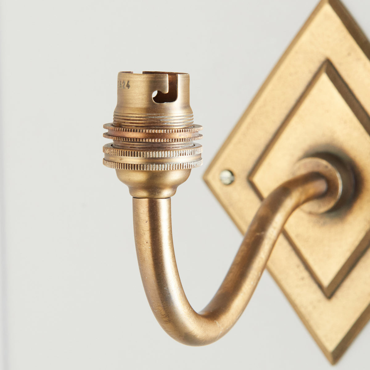 Detail of the ribbed brass lampholder and curving arm of the Diamond Curve wall light against pale panelling