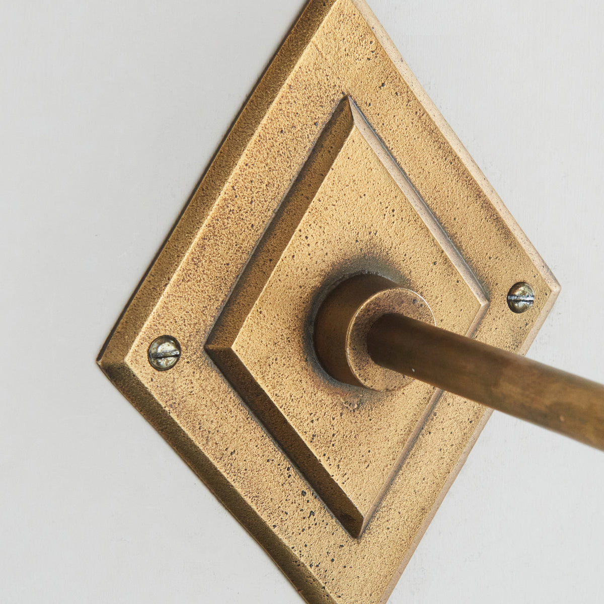 Detail of the aged brass diamond backplate of the Diamond Angle wall light with fixing screws
