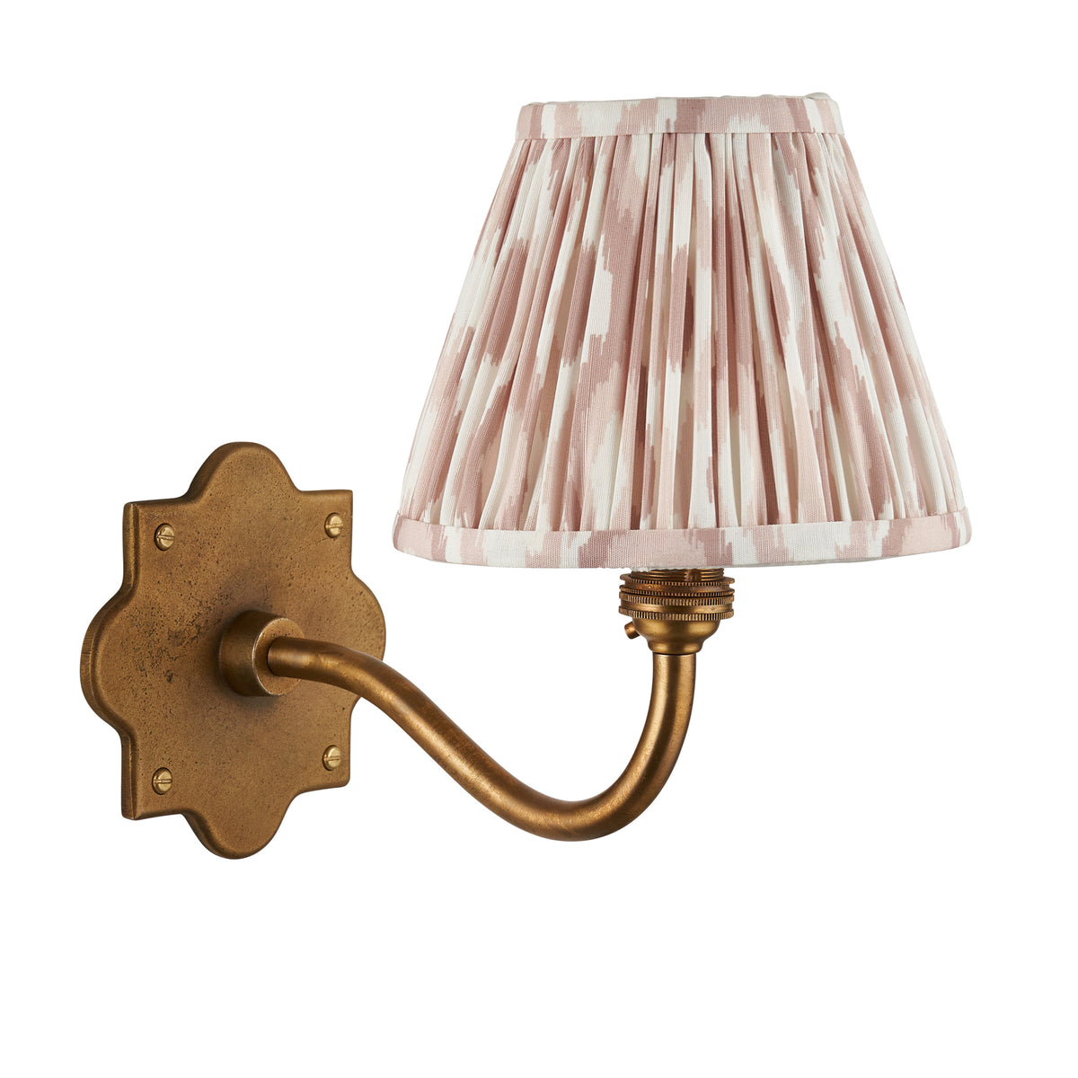 Anvil Curve brass wall light with blush-toned pleated ikat shade against a plain white backdrop