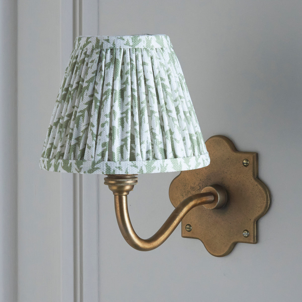 Lit Anvil Curve wall light on grey-white panelling, crisp green leaf-print pleated shade