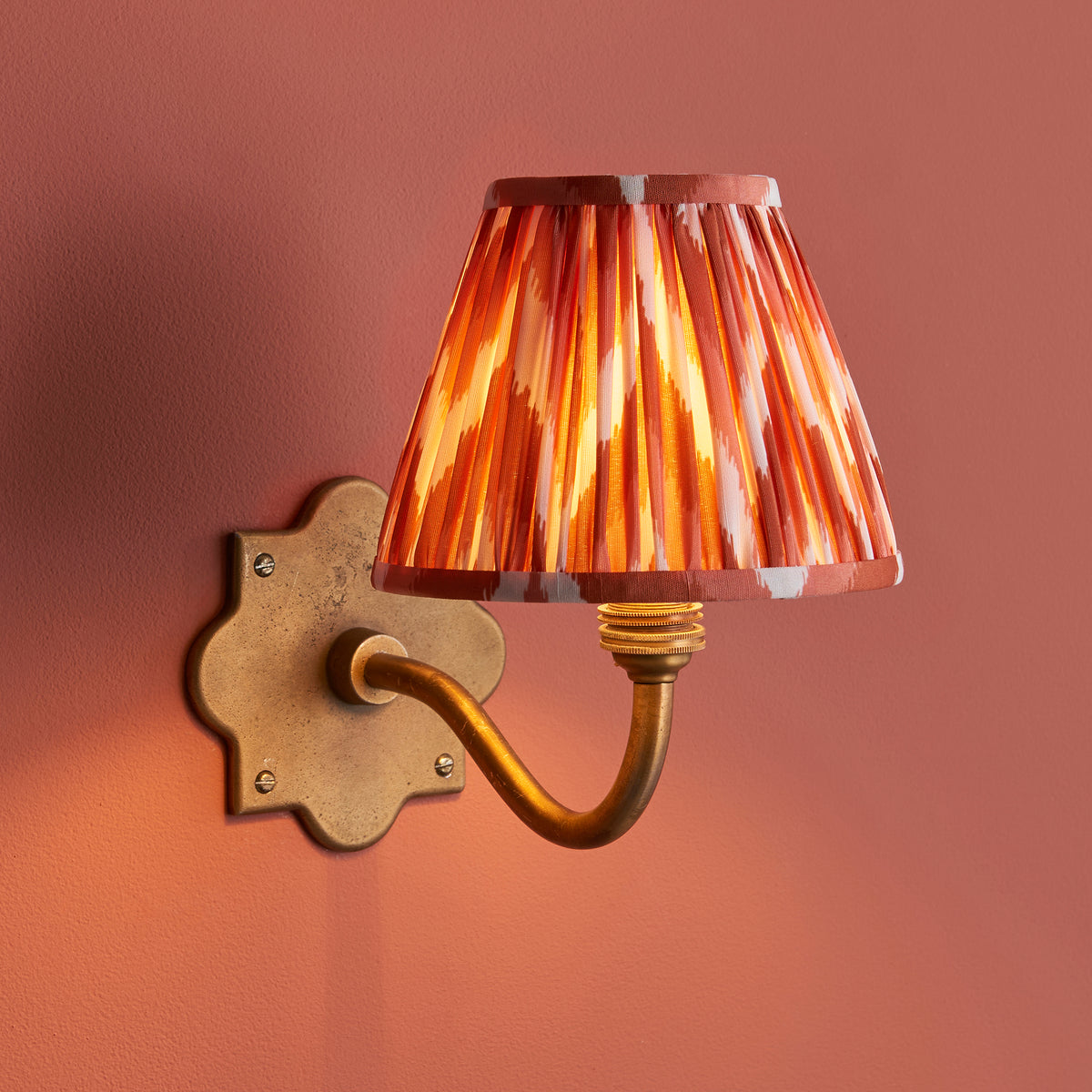 Anvil Curve wall light on a terracotta wall, glowing orange zigzag ikat pleated shade