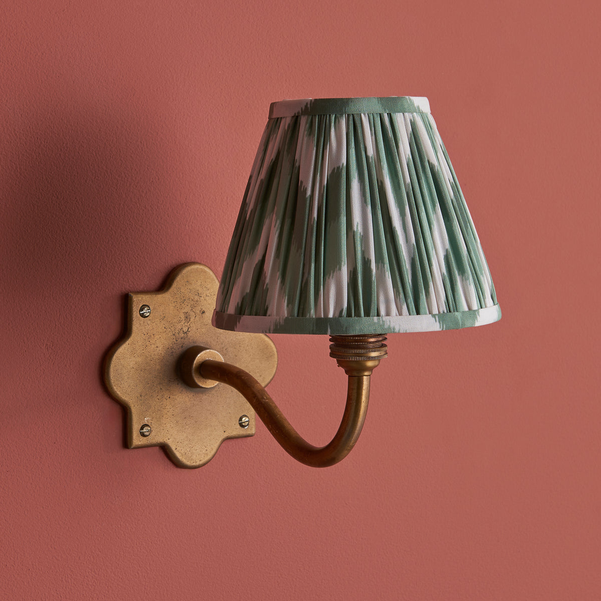 Anvil Curve brass wall light on deep terracotta paint with sage green zigzag ikat pleated shade