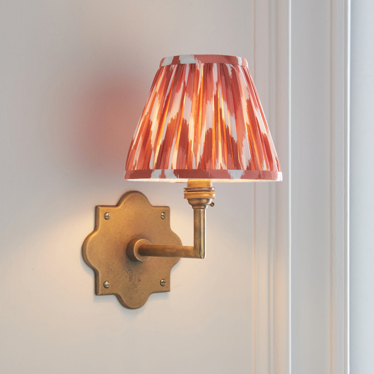 Anvil Angle brass wall light angled on panelling with pink-orange zigzag ikat pleated shade