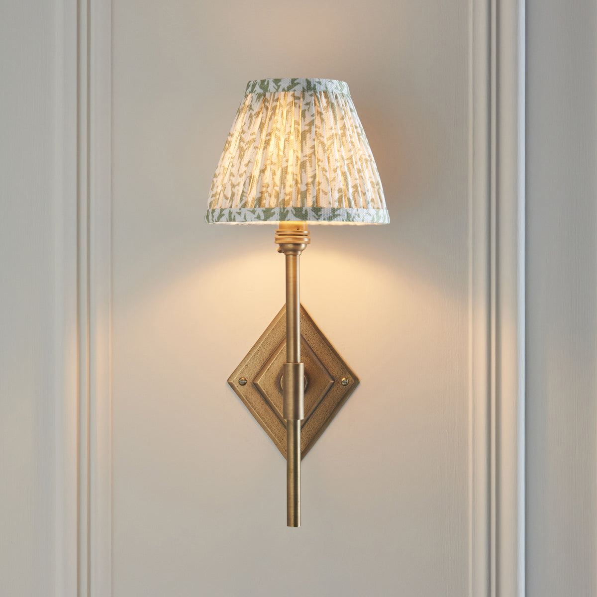 Diamond Tall brass wall light head-on, diamond backplate and slim stem below a leaf-print shade