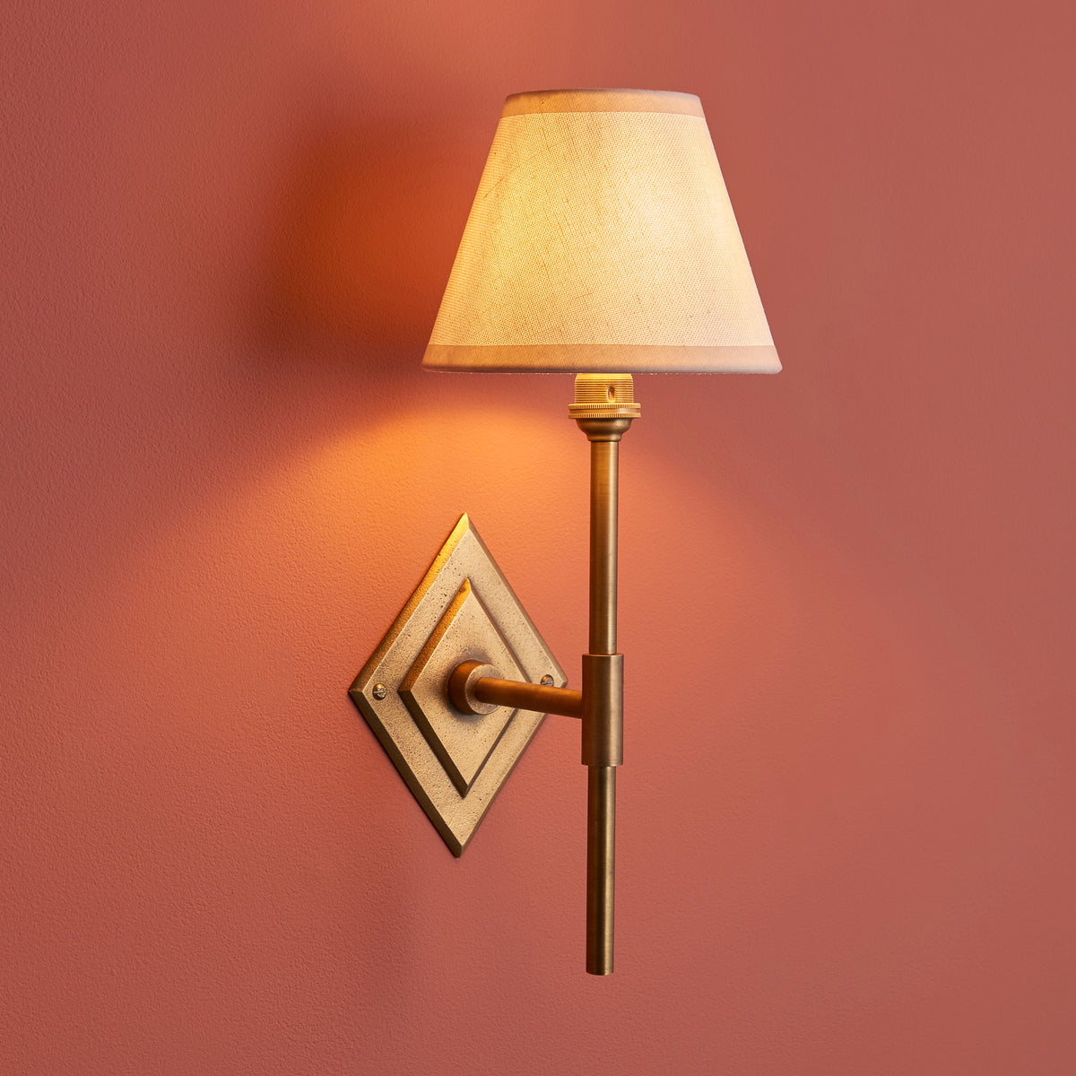 Diamond Tall brass wall light on a terracotta wall, warm-lit cream fabric empire shade