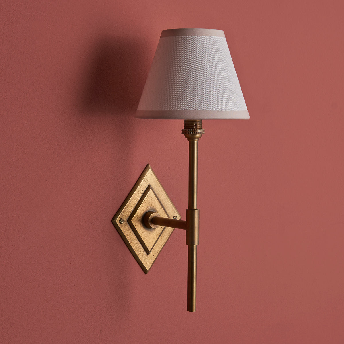 Diamond Tall brass wall light on a deep terracotta wall, unlit white fabric shade and brass stem