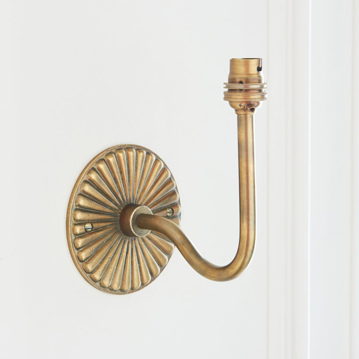 Bare antique brass swan-neck wall fitting with fluted backplate and exposed bulb holder