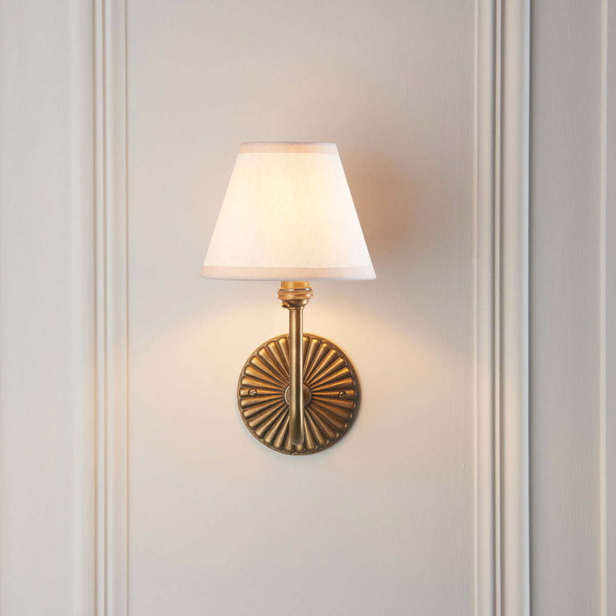 Front view of the Dahlia Swan wall light, fluted brass backplate and white linen tapered shade