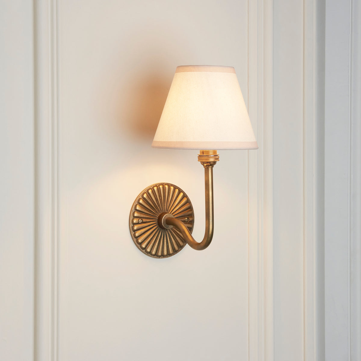 Angled view of the swan-neck antique brass wall light with cream linen empire shade