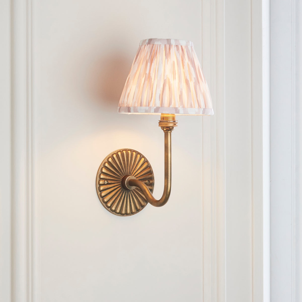 Angled view of the swan-neck brass wall light with soft beige ikat pleated fabric shade