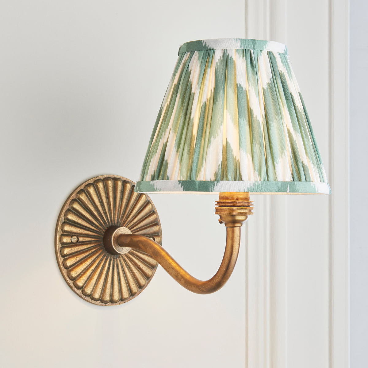 Angled view of the Dahlia Curve brass wall light with green and cream ikat pleated shade