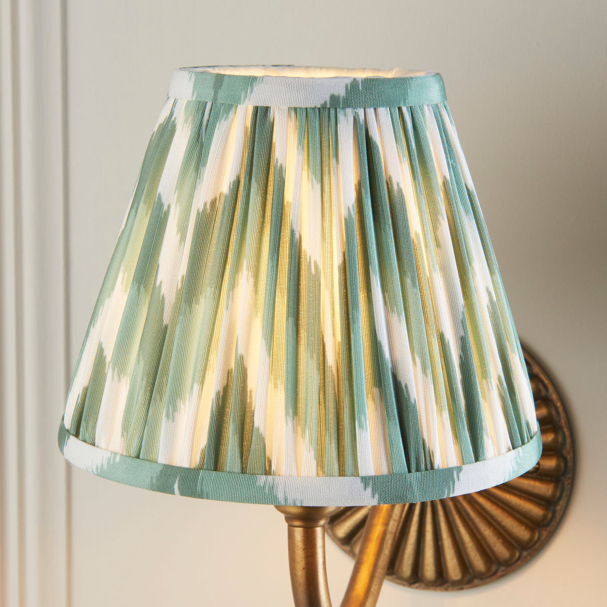 Close-up of the lit green zigzag ikat pleated shade on the Dahlia Curve brass wall light