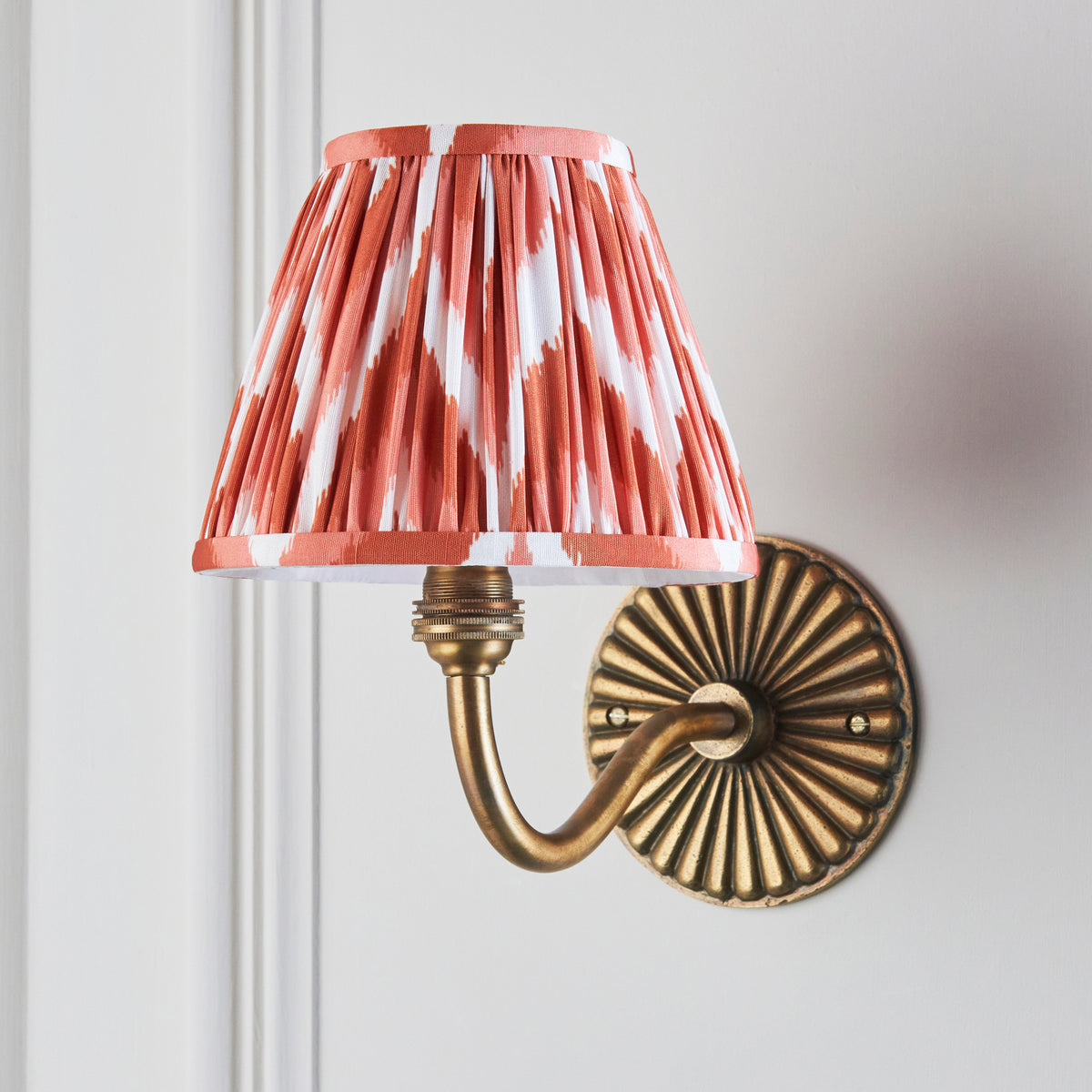 Dahlia Curve brass wall light seen from the side, orange zigzag shade against cream panelling