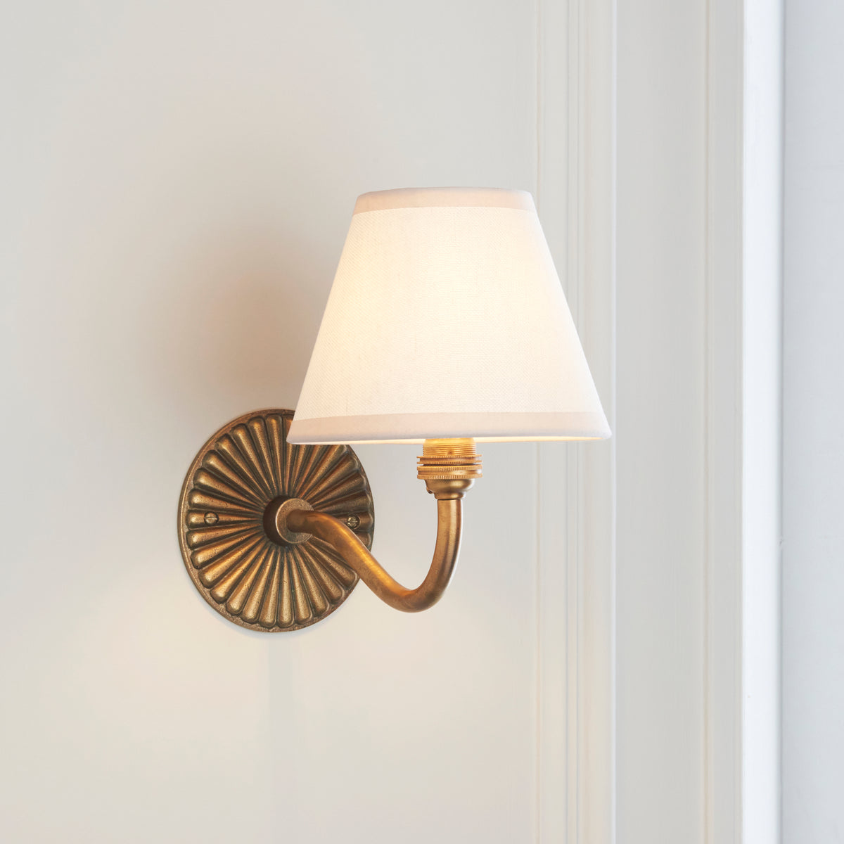 Angled shot of the antique brass Dahlia Curve & Ivy wall light with softly glowing ivory shade