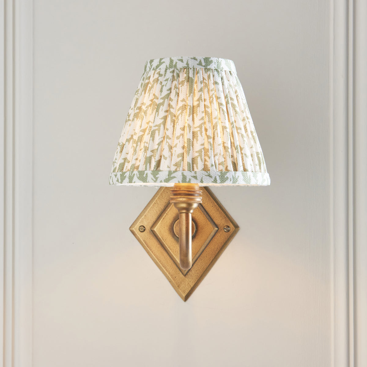 Front view of the Diamond Curve sconce, diamond brass backplate below a glowing leaf print shade