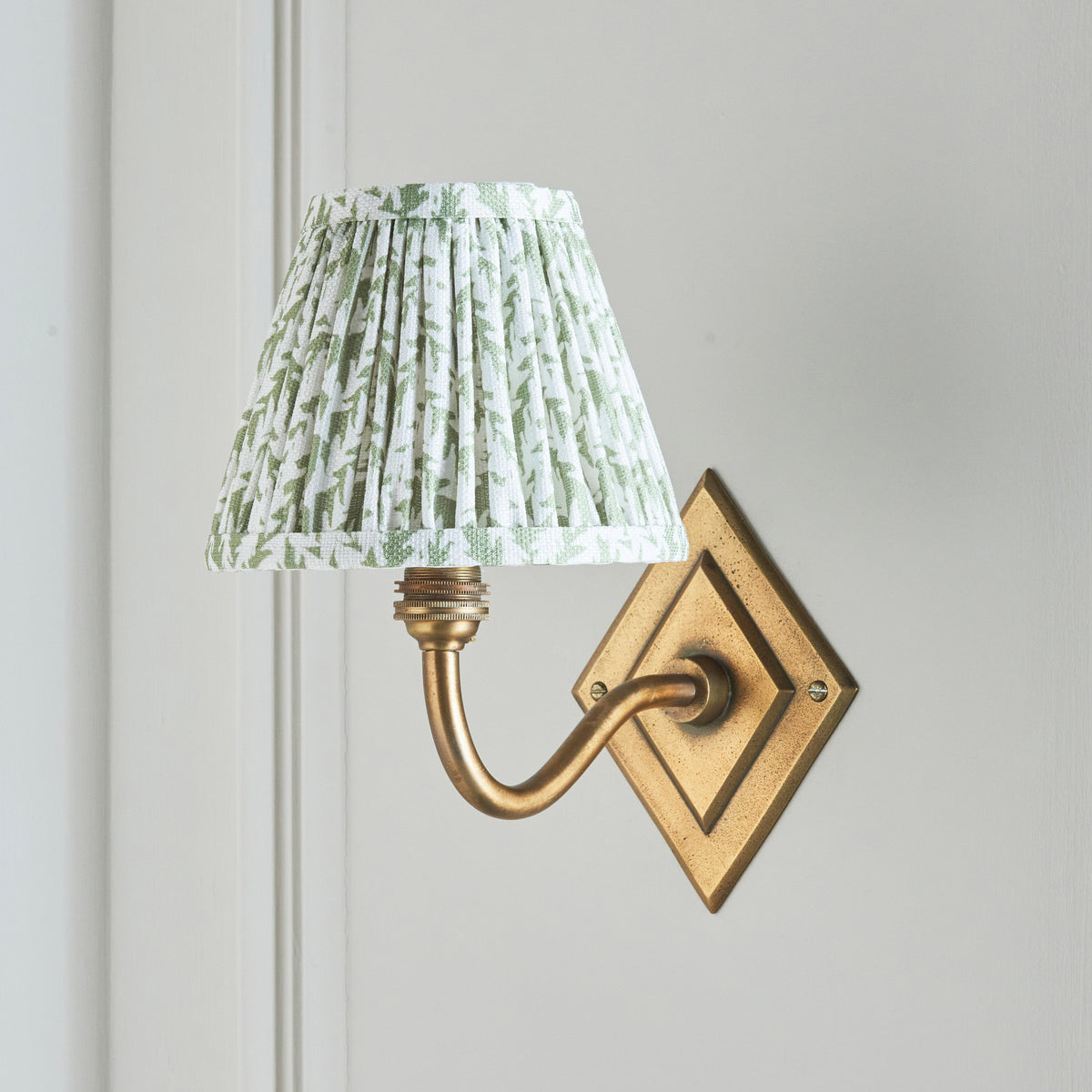 Side view of the Diamond Curve brass wall light, green leaf shade against cream wall panelling