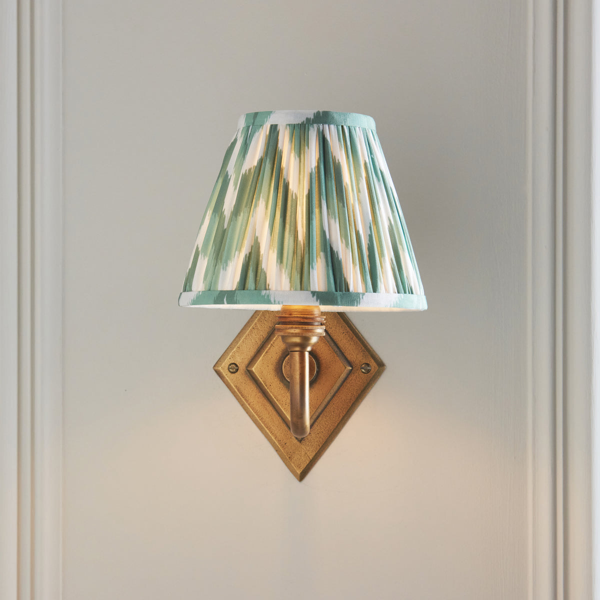 Front view of the Diamond Curve sconce, brass diamond backplate under a glowing green ikat shade