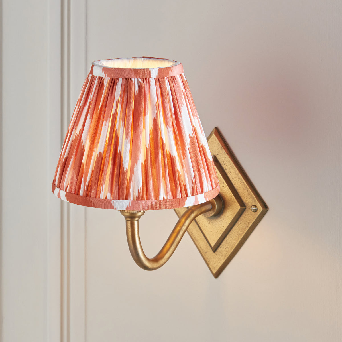 Close view of the pleated orange zigzag shade above the curved brass arm and diamond backplate