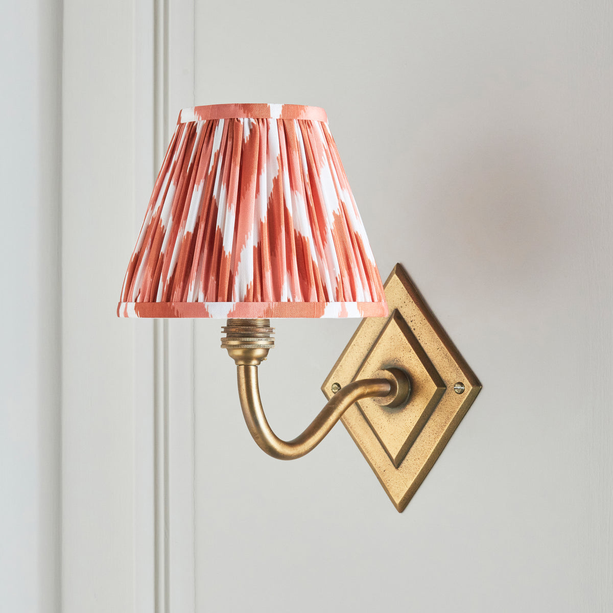 Side view of the Diamond Curve wall light, coral zigzag shade against cream wall panelling