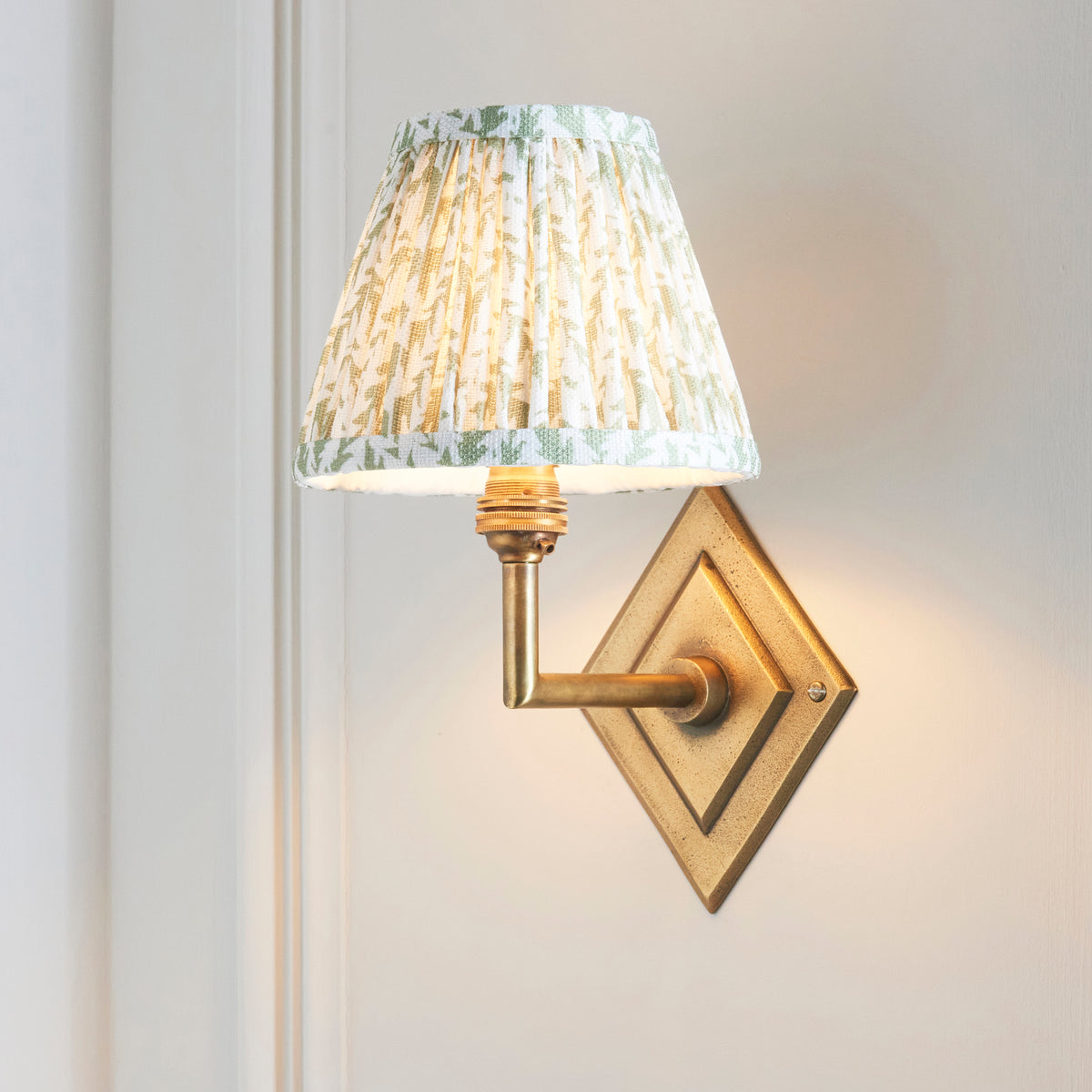 Diamond Angle brass wall light with green leaf pleated shade, angled view on a panelled white wall