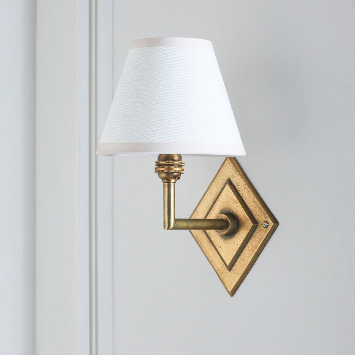 Side view of the Diamond Angle & Ivy brass wall light with its crisp white tapered shade