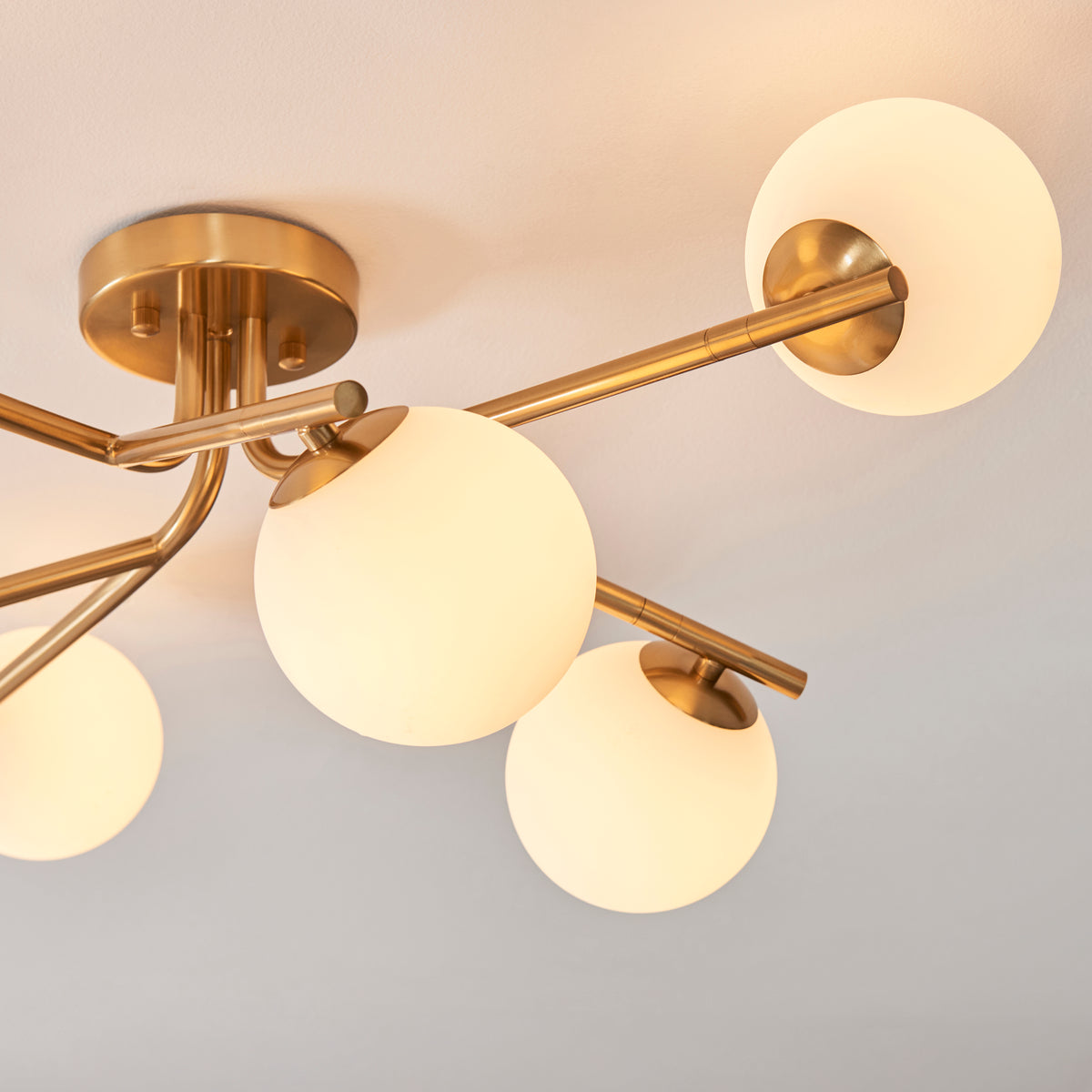 Angled view of the Aaron semi flush light showing brass arms and lit opal glass spheres