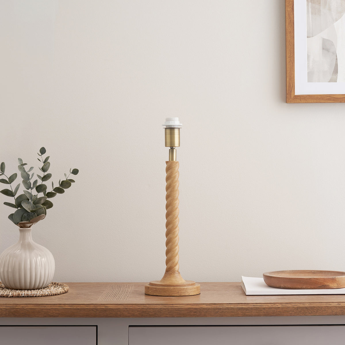 Twist oak effect table lamp base on a wooden sideboard beside a ribbed vase of eucalyptus
