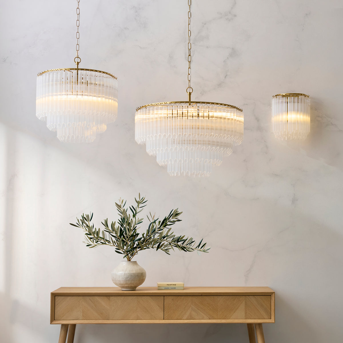 Two Montpellier ribbed glass chandeliers and a wall light above a wooden console with olive branches