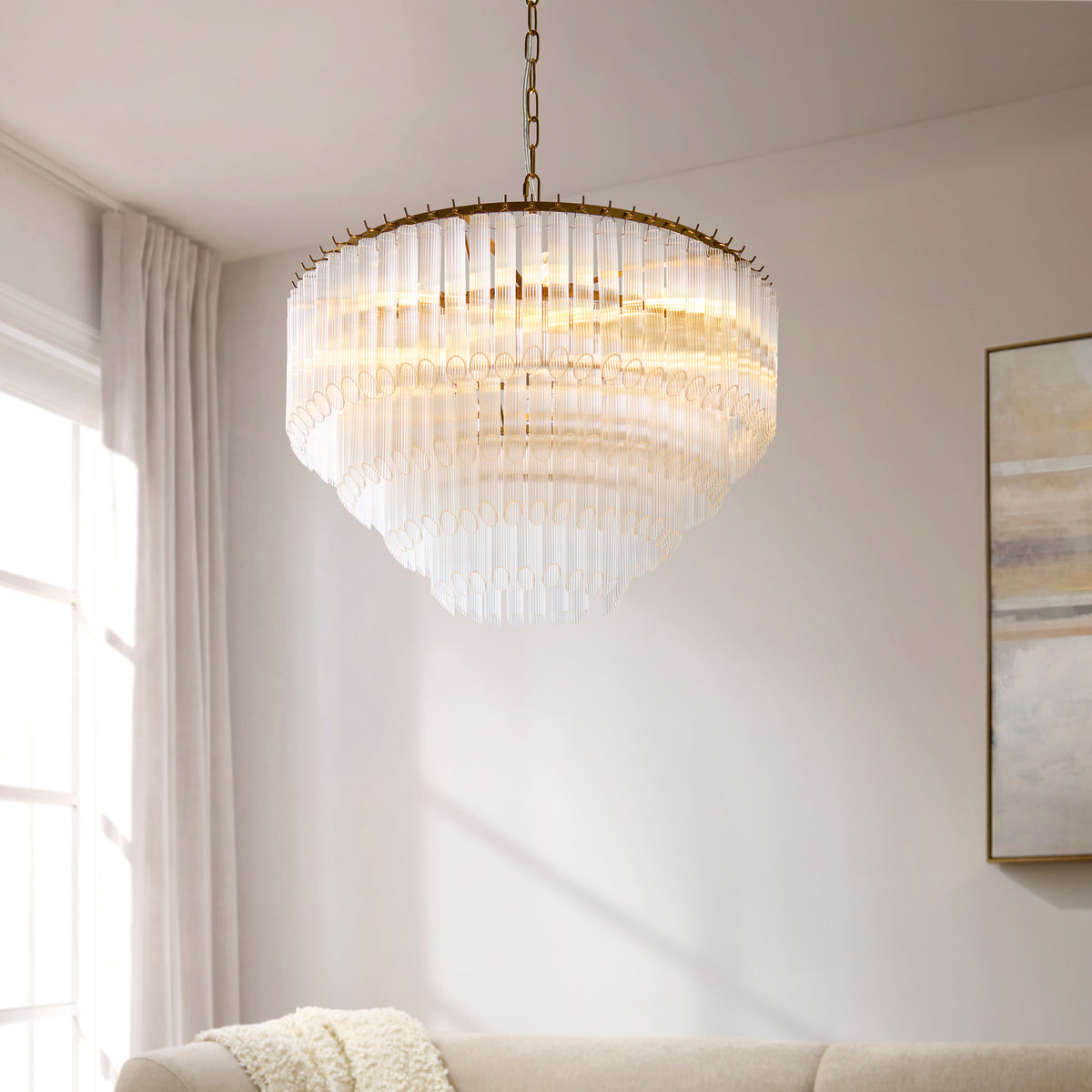 Lit Montpellier ribbed glass chandelier above a cream sofa and soft abstract wall art