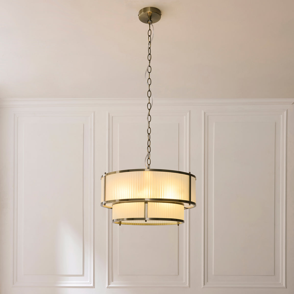 Ridgeton antique brass pendant glowing against white wall panelling on a long chain