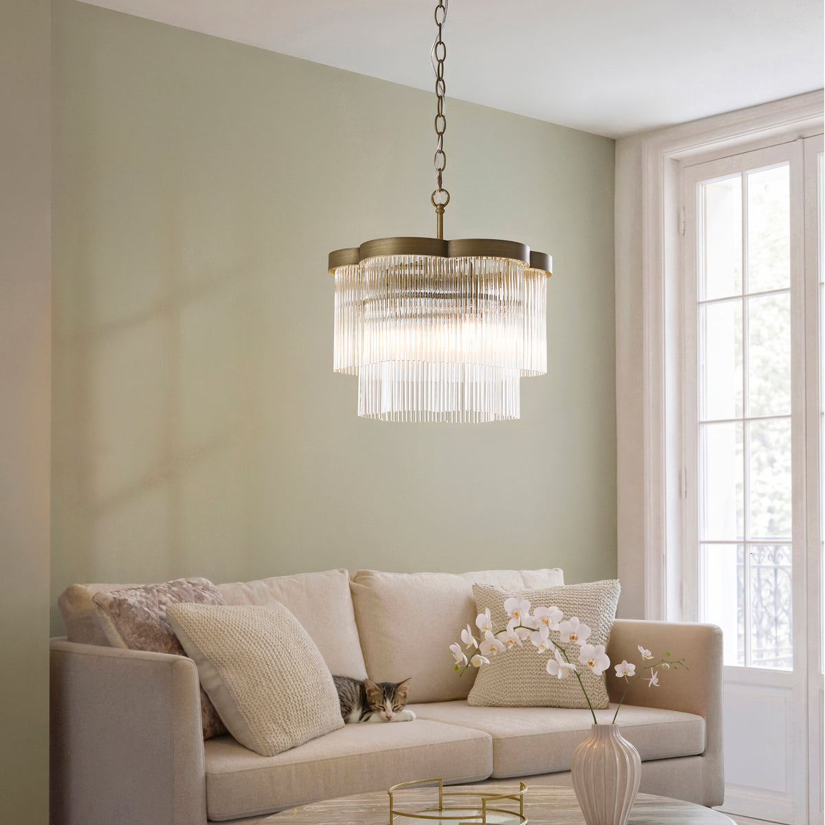 Lucille glass rod chandelier lit above a cream sofa in a sage green living room