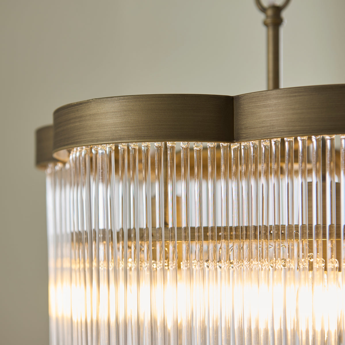 Close-up of the Lucille chandelier's brushed brass rim above rows of clear glass rods