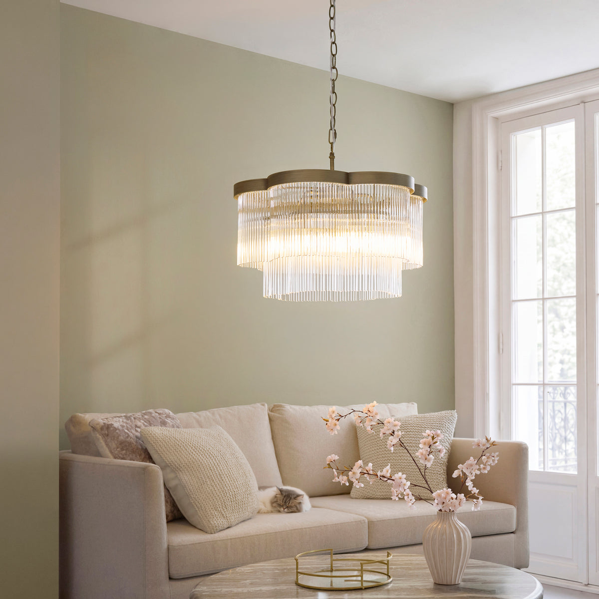 Lucille 5 light glass rod chandelier lit above a cream sofa in a sage green sitting room