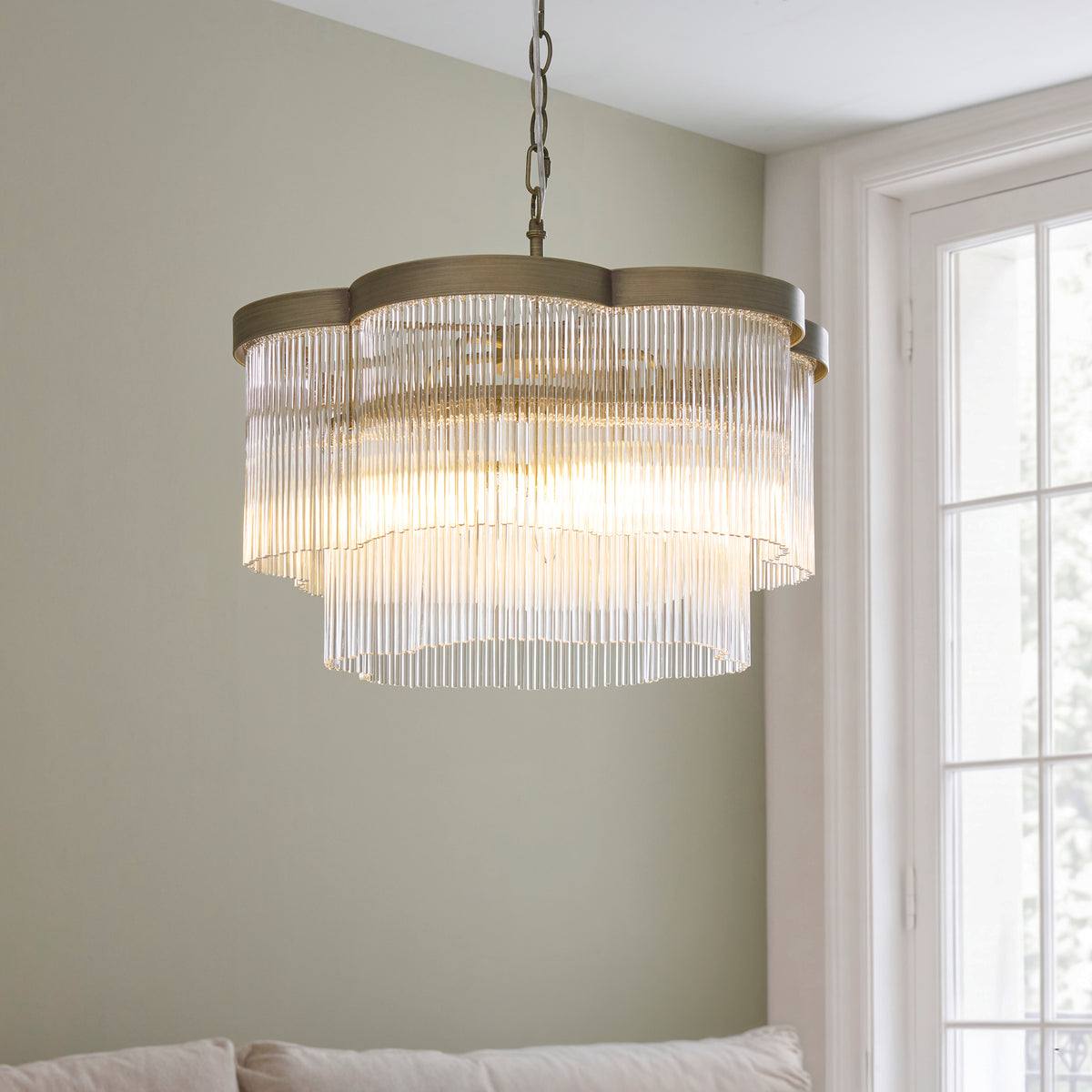 Lucille chandelier glowing beside a bright window in a sage green room