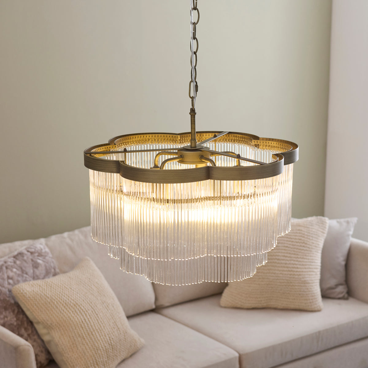 Lucille chandelier seen from below, its scalloped brass frame framing lit glass rods