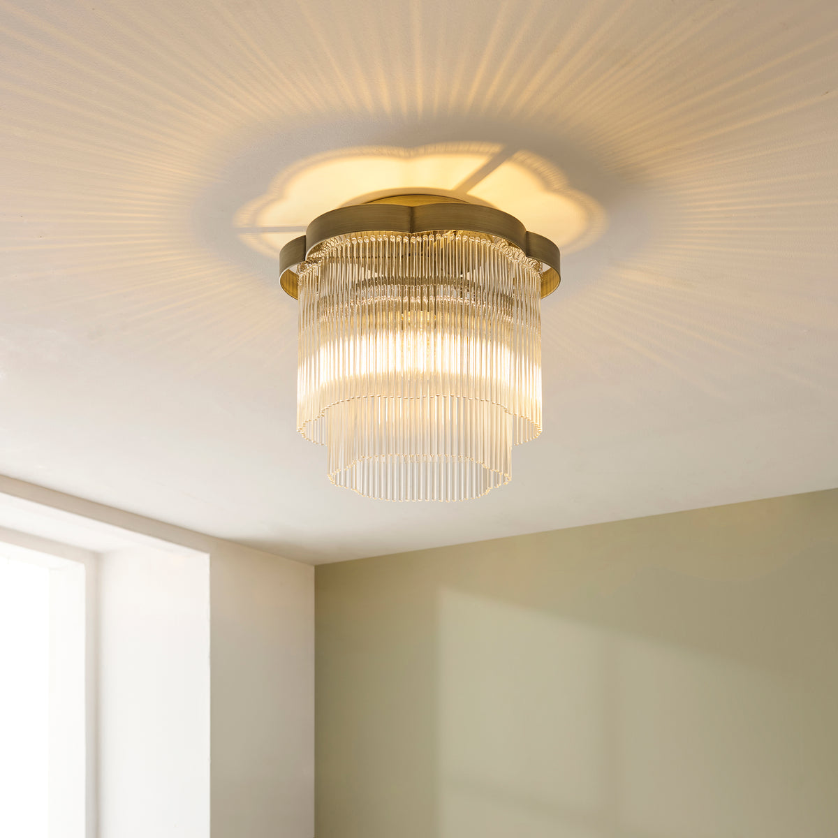 Lucille flush ceiling light lit on a white bedroom ceiling, casting starburst patterns beside a window