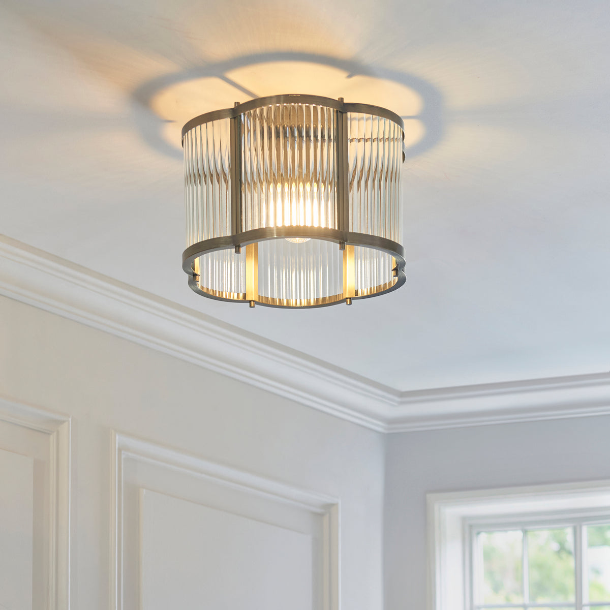 Ridgeton Scallop ceiling light lit on a white ceiling above coving in a grey panelled room