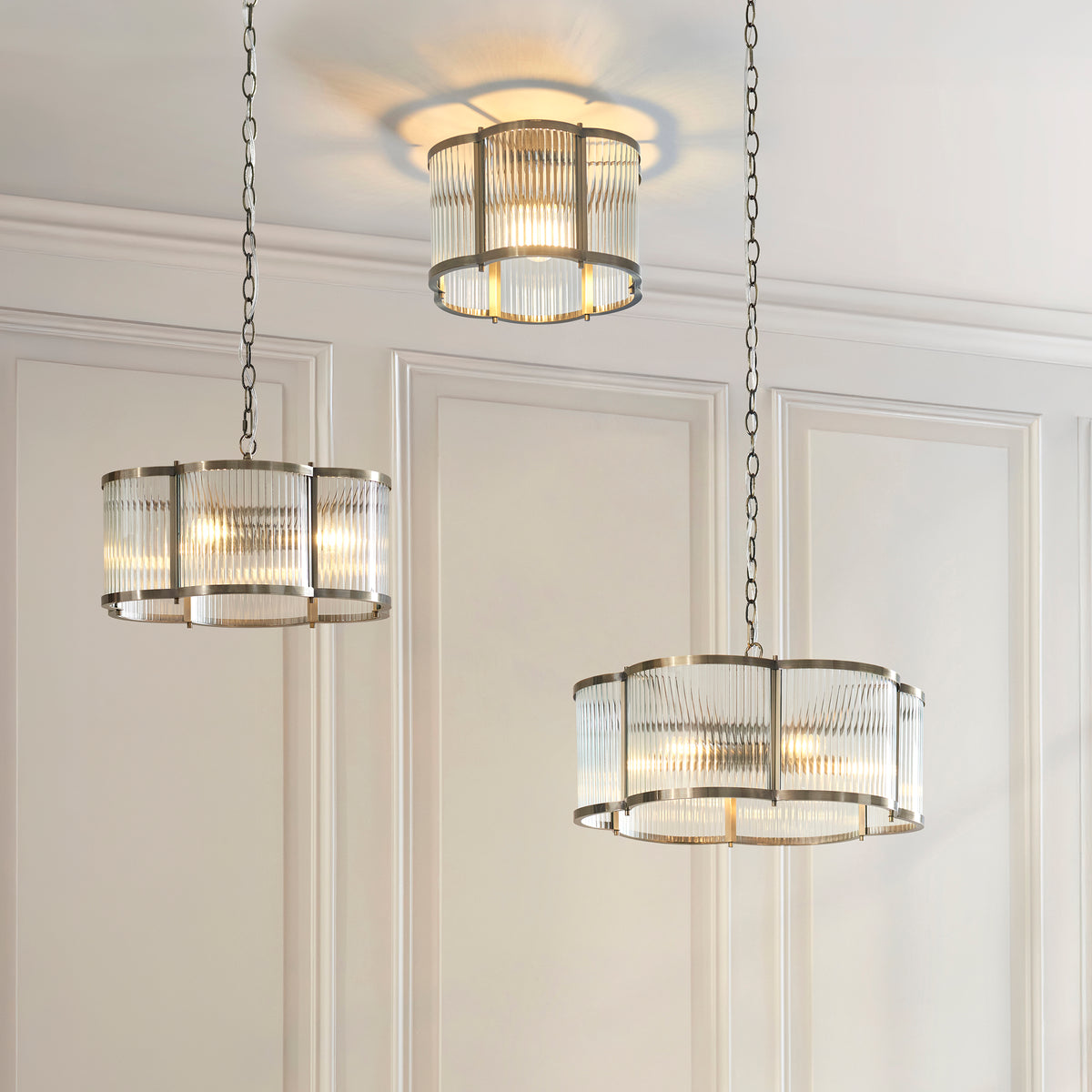 Three lit Ridgeton antique brass ribbed glass fittings, including the flush light, on a panelled wall