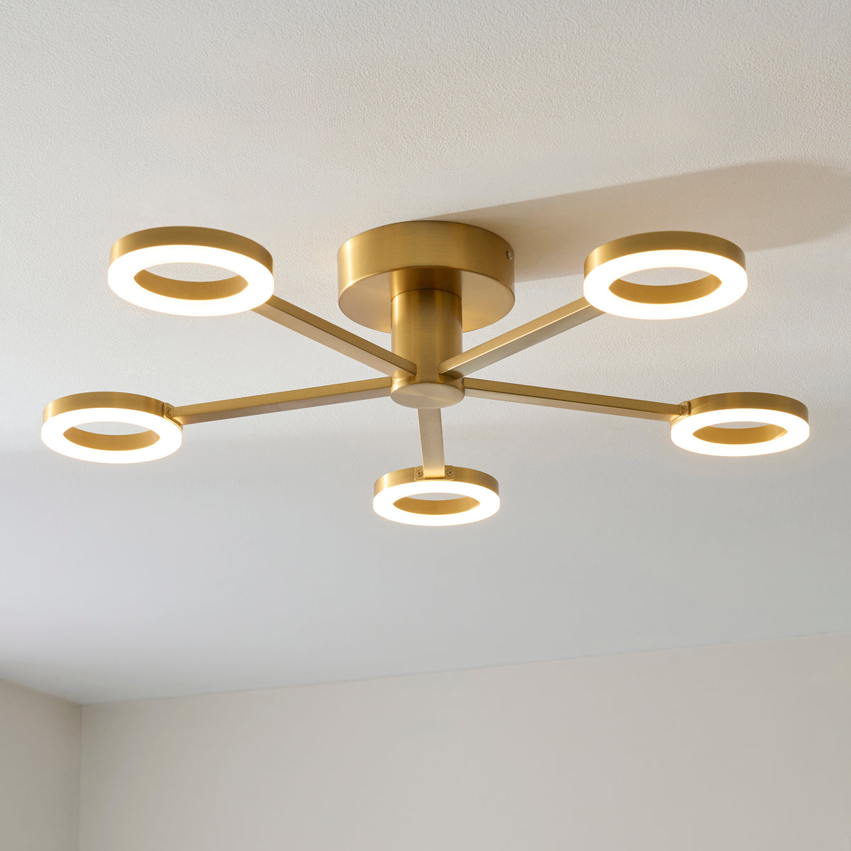 Angled view of the lit Scout ceiling light showing five warm brass LED rings and central drum