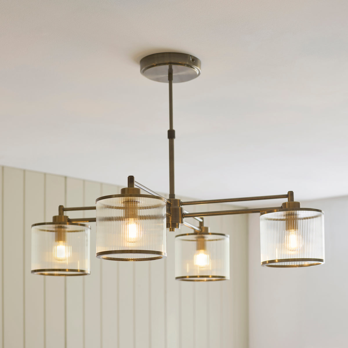 Ridgeton four-light chandelier in antique brass with ribbed glass shades in a panelled room