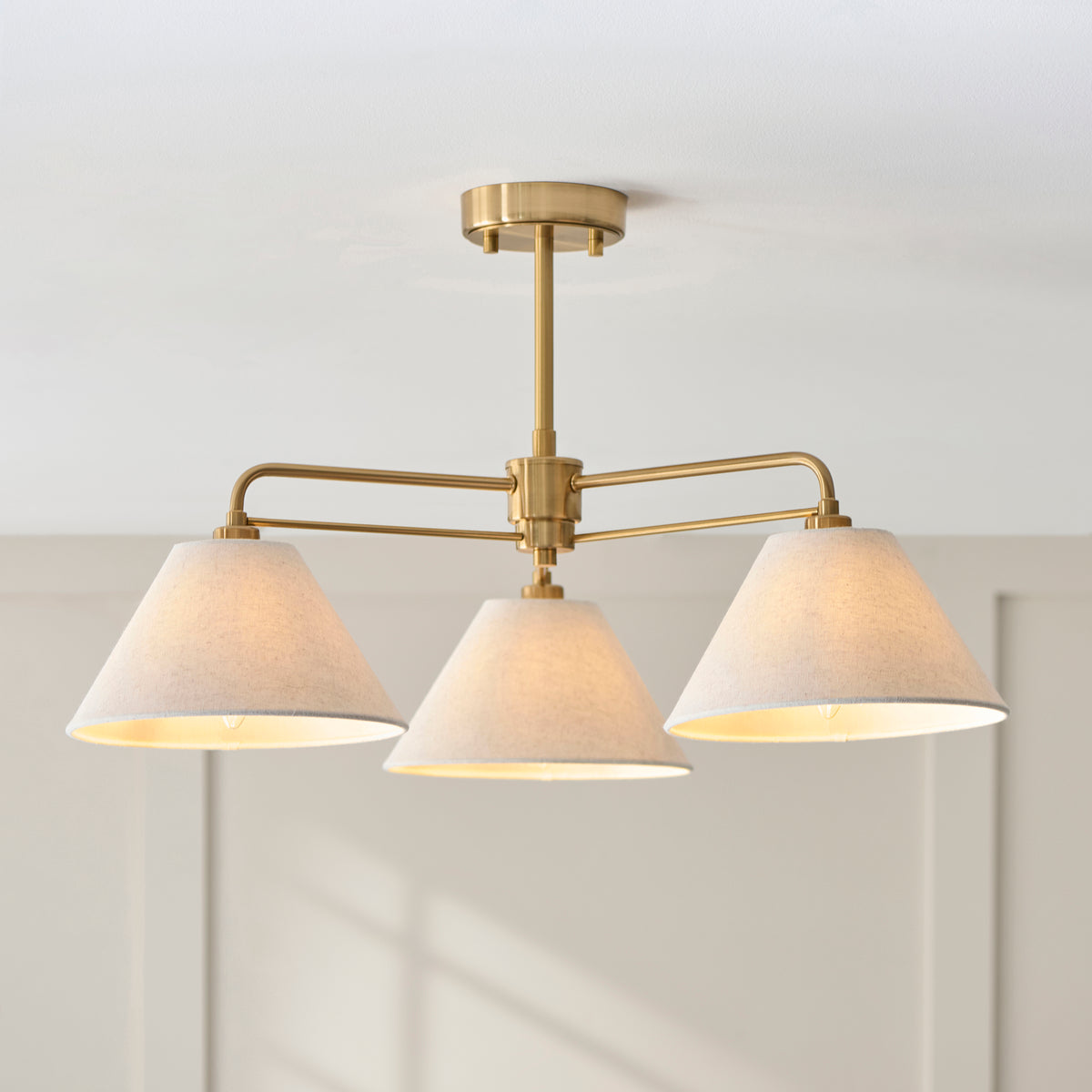 Wallbridge aged brass semi flush ceiling light glowing against white panelled walls