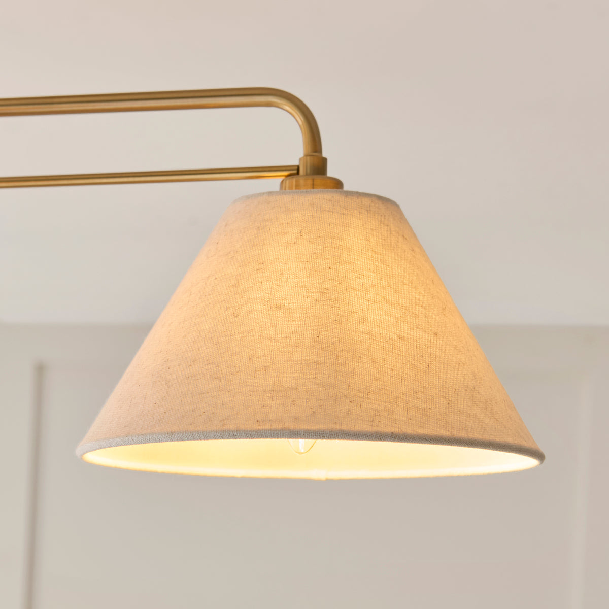 Close view of one tapered oatmeal linen shade on the Wallbridge light's aged brass arm