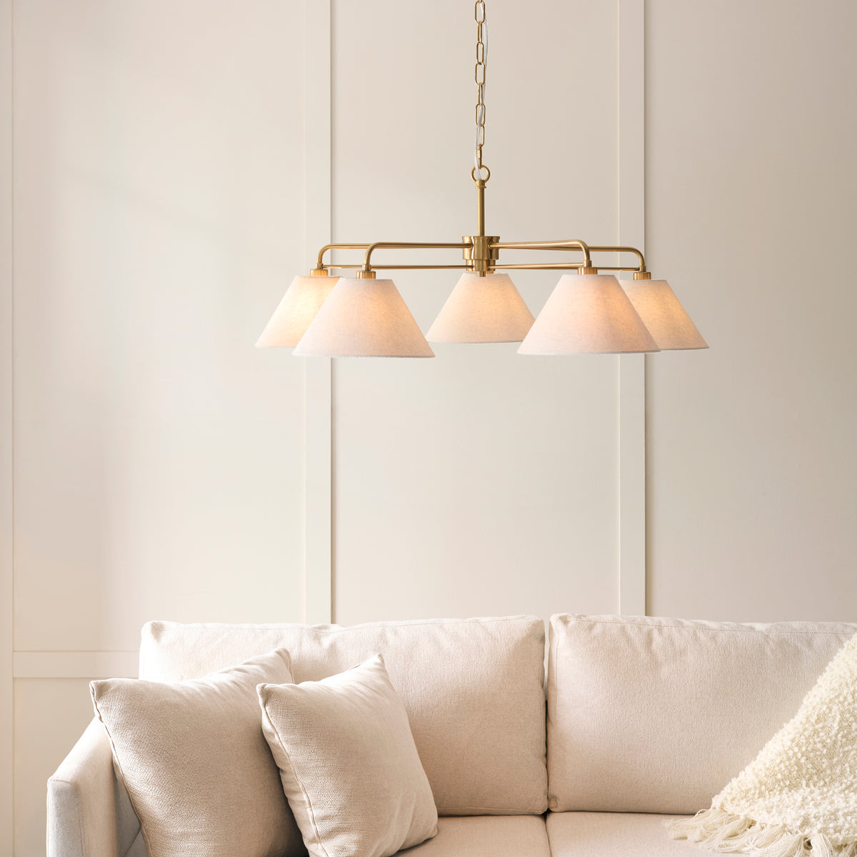 Wallbridge brass five-light pendant lit above a cream sofa in a panelled living room