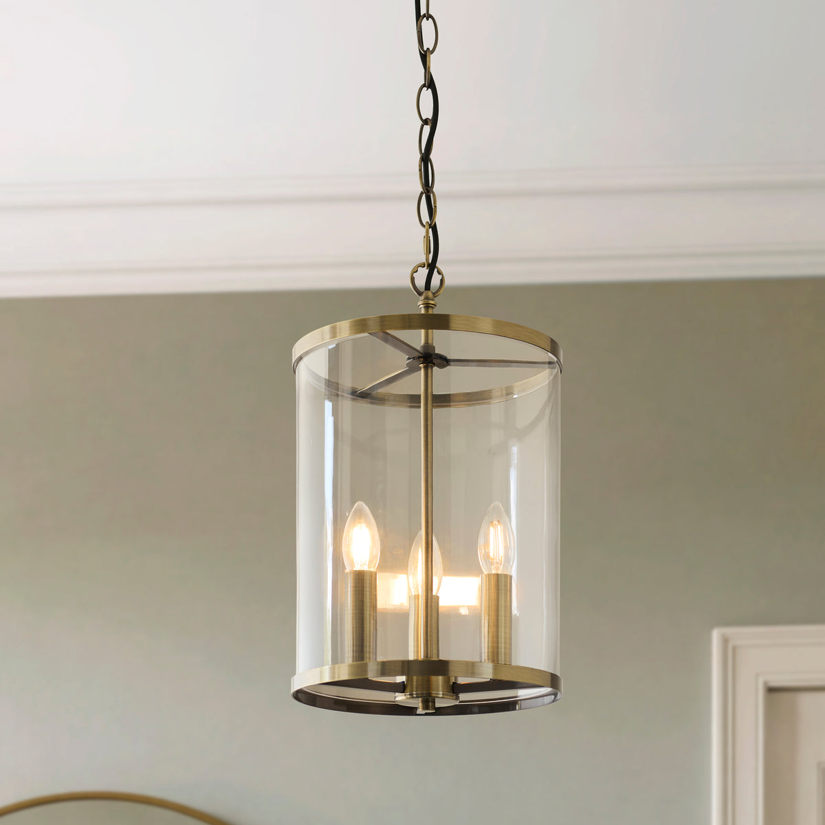Hebden antique brass lantern pendant lit with three candle bulbs against a soft green wall
