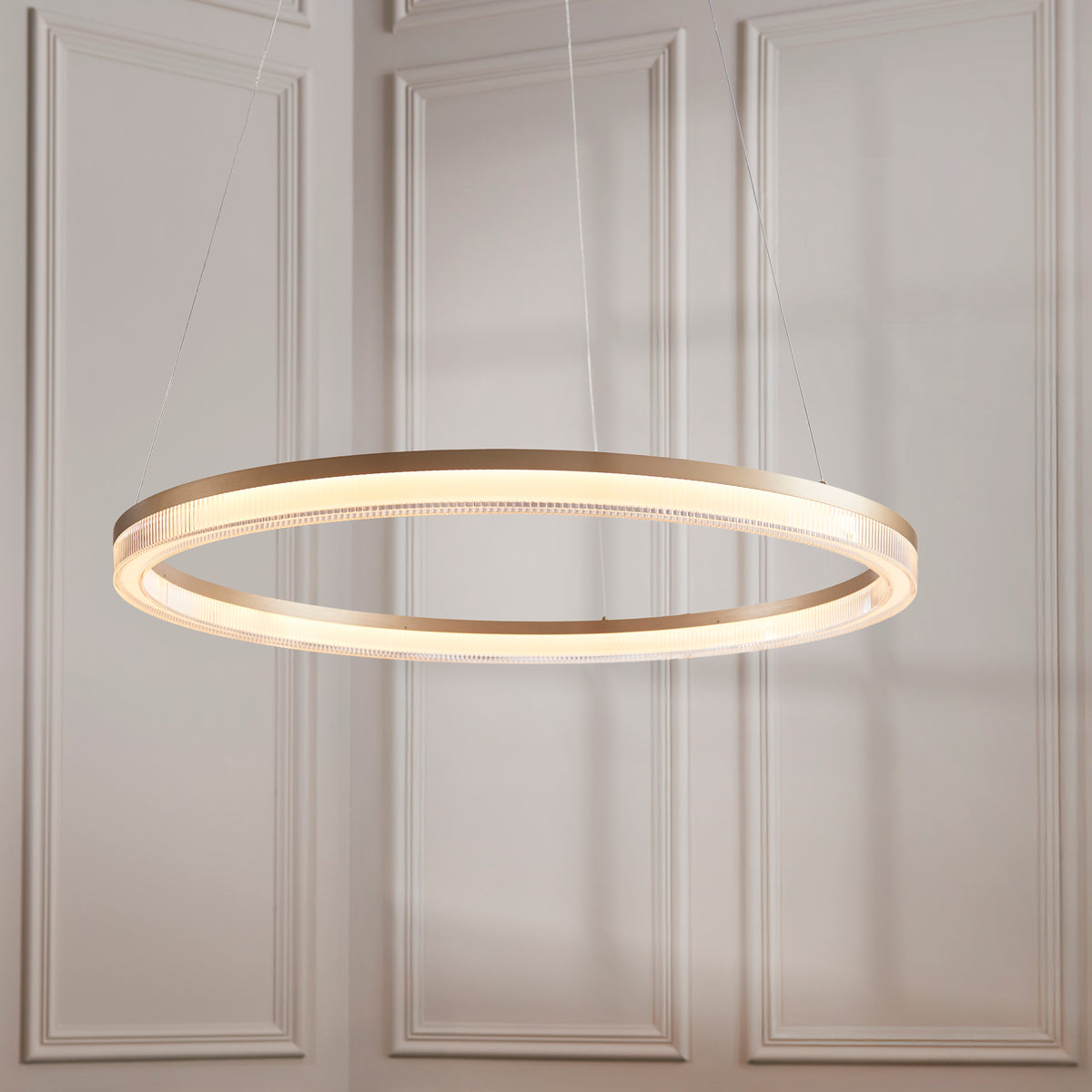 Lansina brushed gold LED ring pendant lit against pale panelled walls