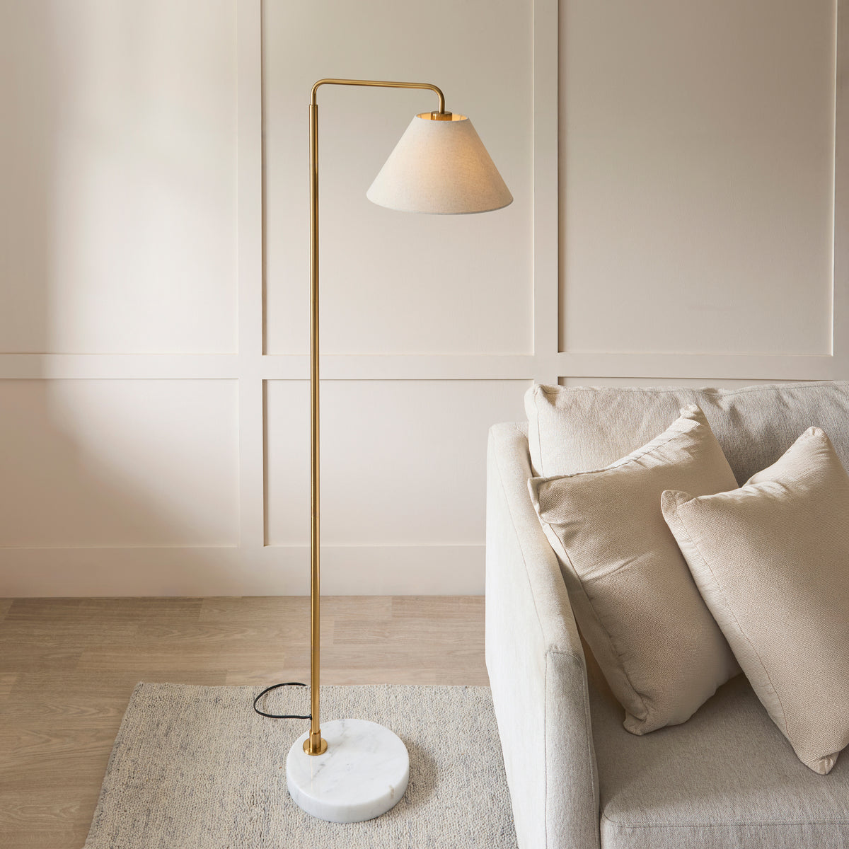 Wallbridge floor lamp with glowing linen shade next to a pale sofa and cushions