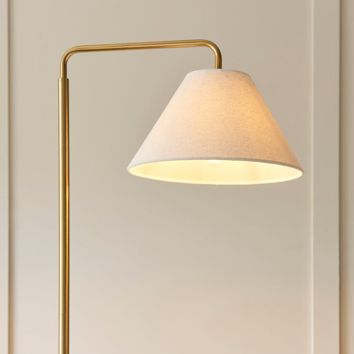 Wallbridge floor lamp's lit cream linen shade angled against a panelled wall