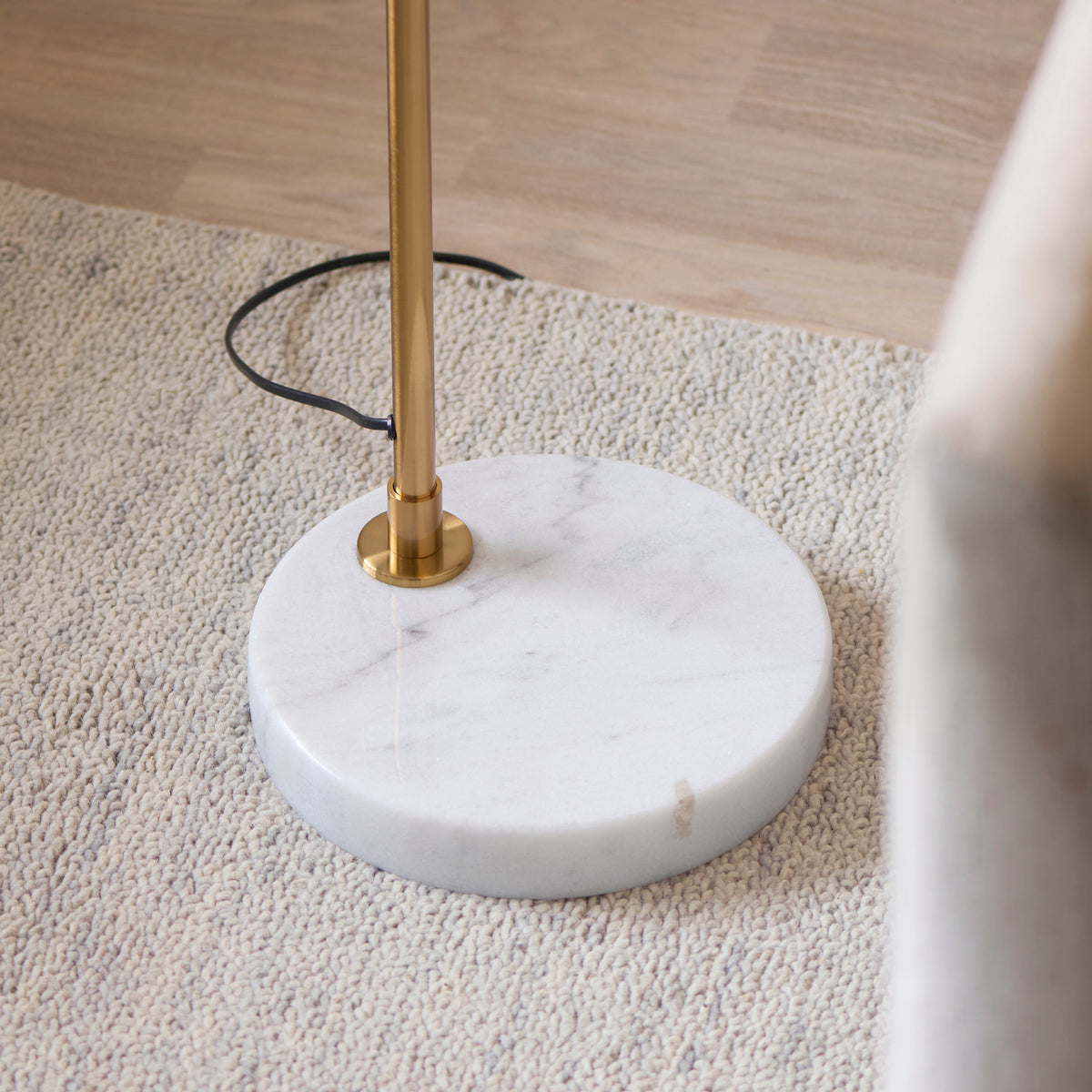 White marble disc base and brass stem of the Wallbridge floor lamp on a textured rug